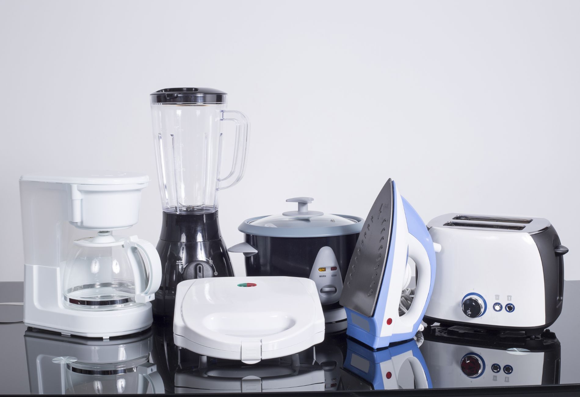 Vari elettrodomestici da cucina su un piano di lavoro riflettente, tra cui frullatore, tostapane e ferro da stiro.