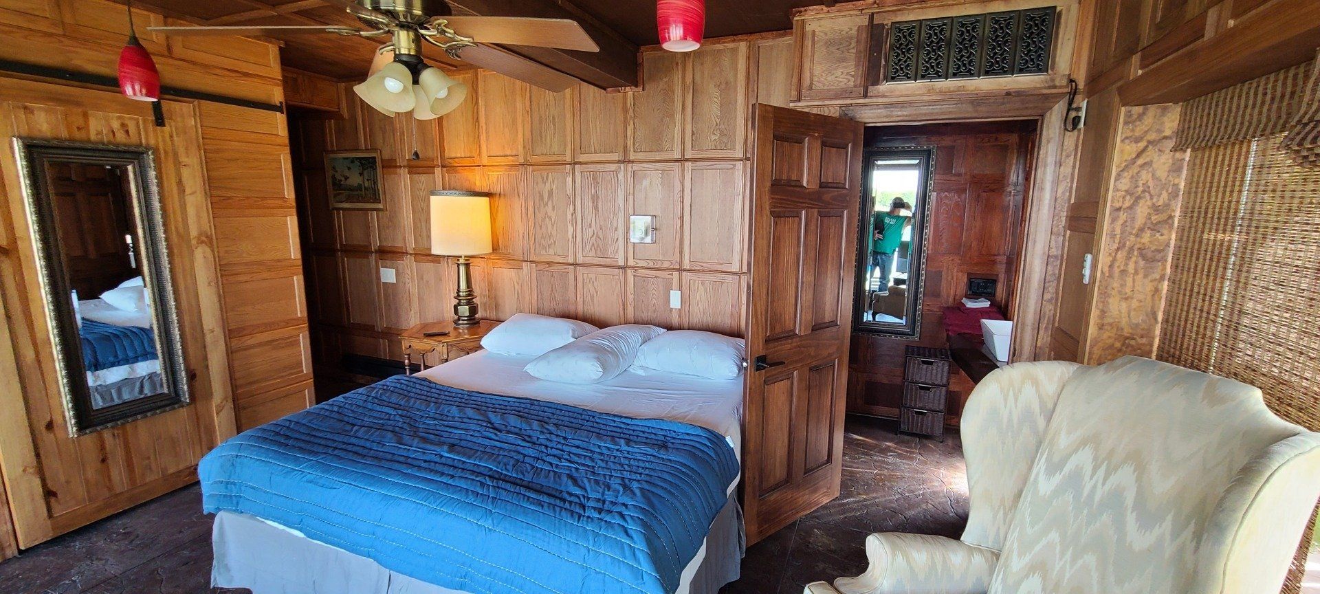 A bedroom with a bed , chair , mirror and ceiling fan.