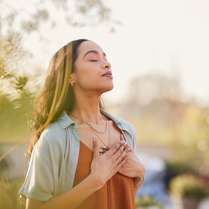 A woman is standing with her eyes closed and her hands on her chest.