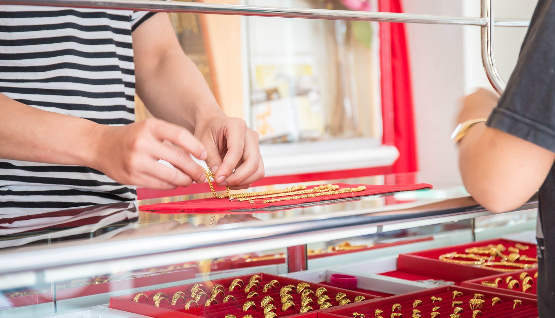 Person examining gold jewelry at a store counter; display case of gold items in foreground.