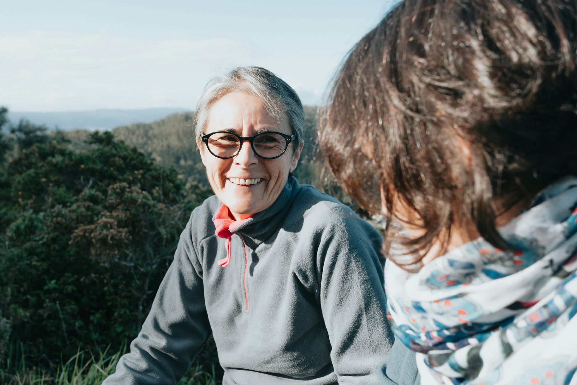 Two women are sitting on top of a hill talking to each other.