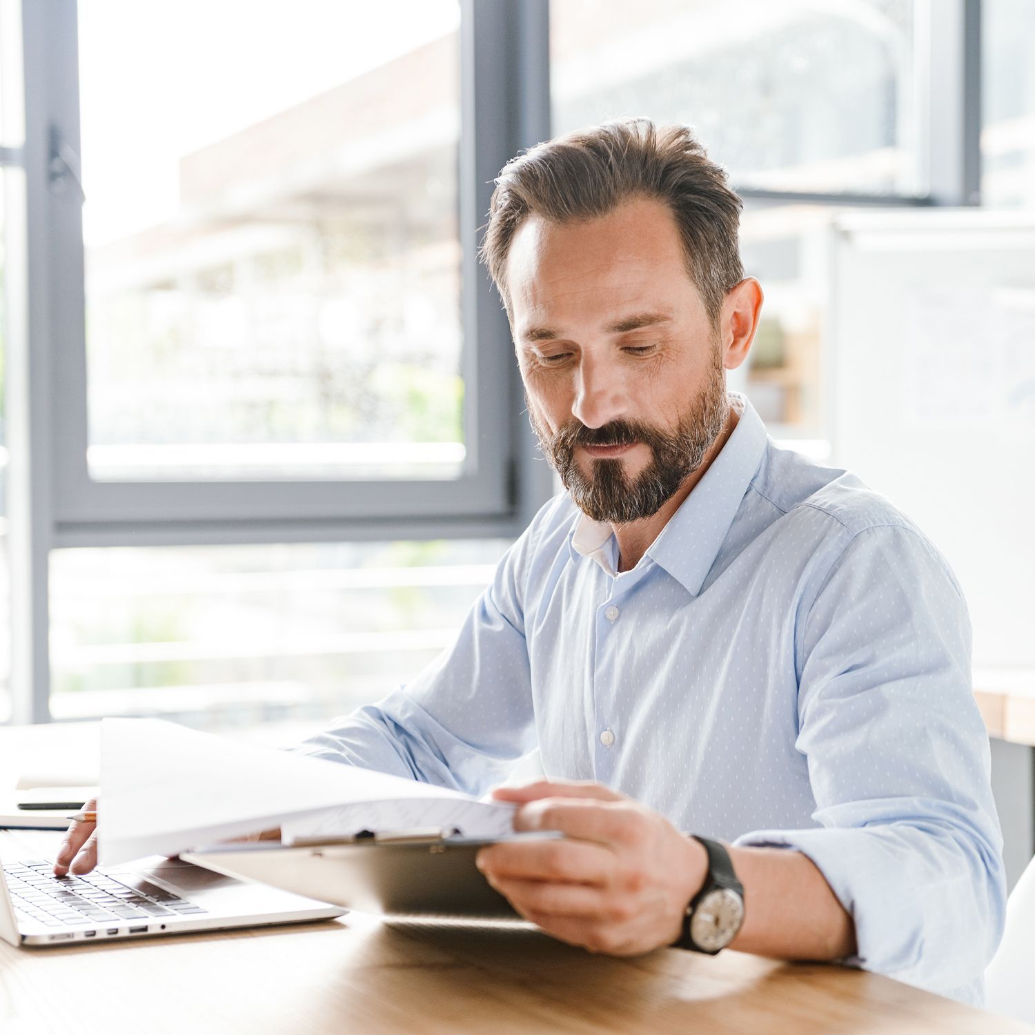 A man with a beard is sitting at a table using a tablet computer.