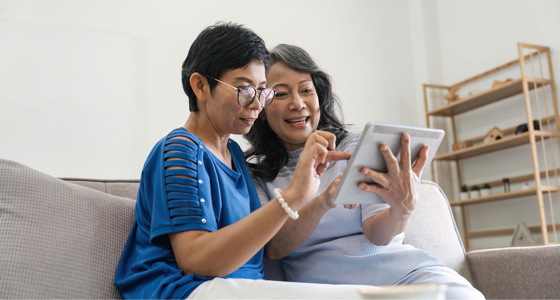 Two women are sitting on a couch looking at a tablet.