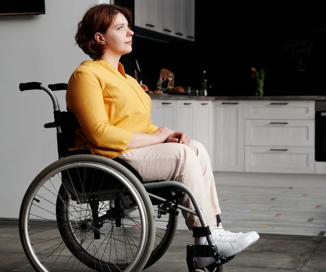 A woman is sitting in a wheelchair in a kitchen.