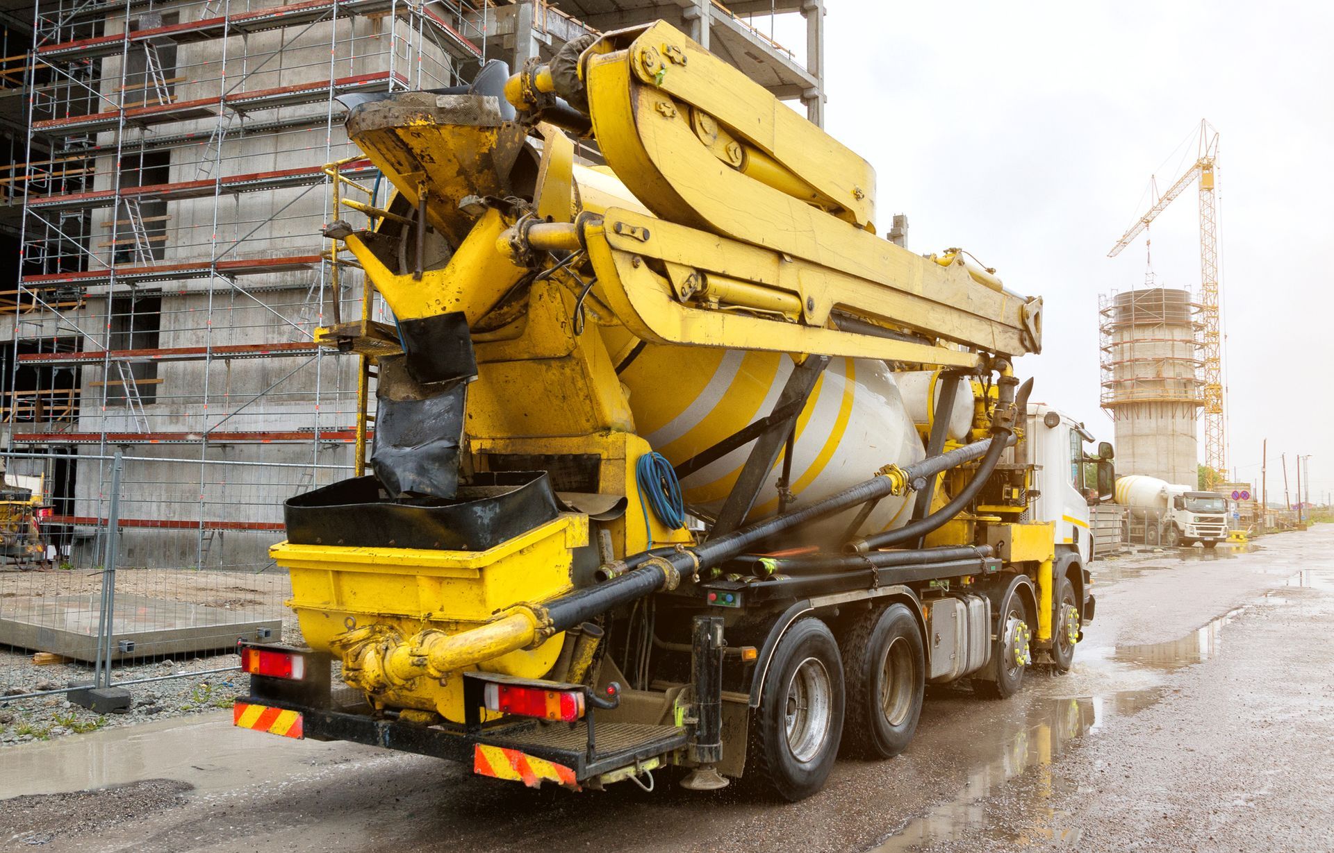 Yellow concrete mixer truck mixes cement in front of a construction site. Yellow concrete mixer truck mixes cement in front of a construction site.