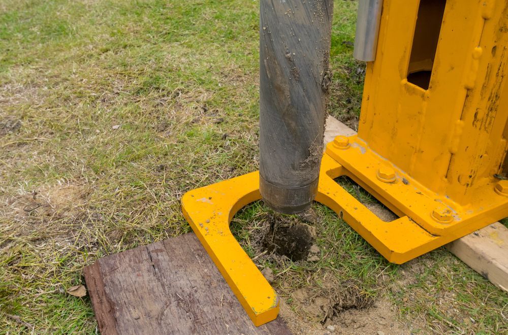 A Yellow Drill Is Sitting In The Grass Next To A Rock — PGI North QLD In Ingham, QLD