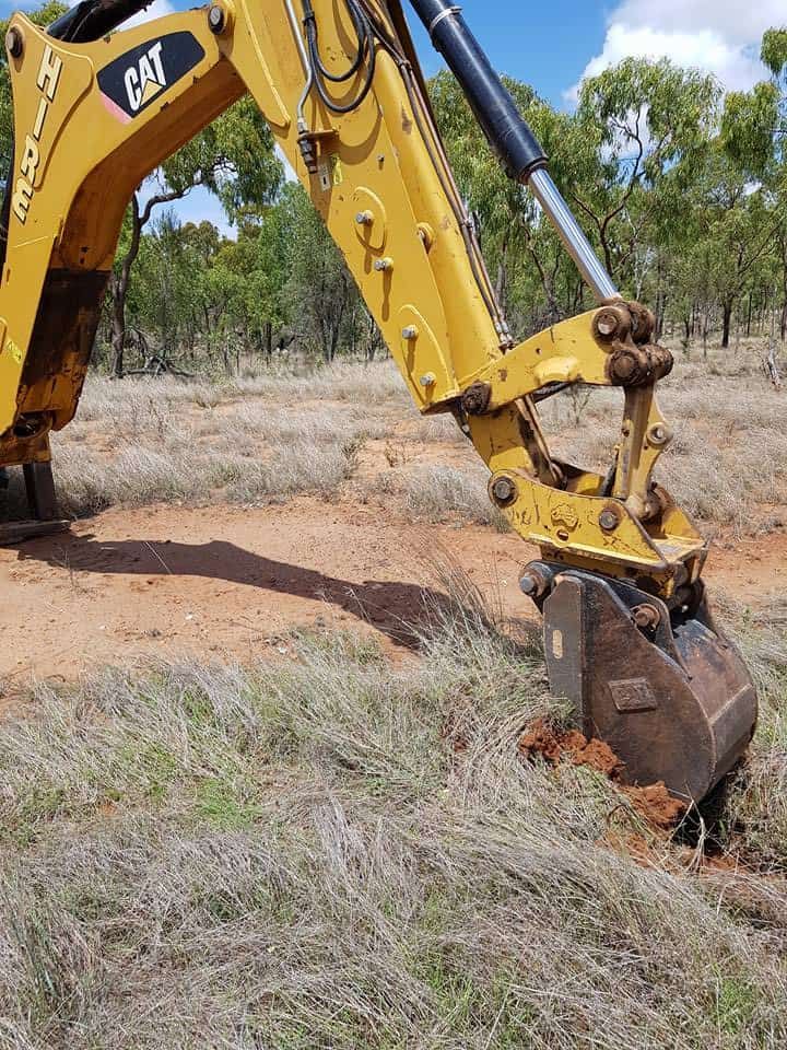 A Yellow Excavator Is Digging A Hole In The Ground In A Field — PGI North QLD In Charters Towers, QLD