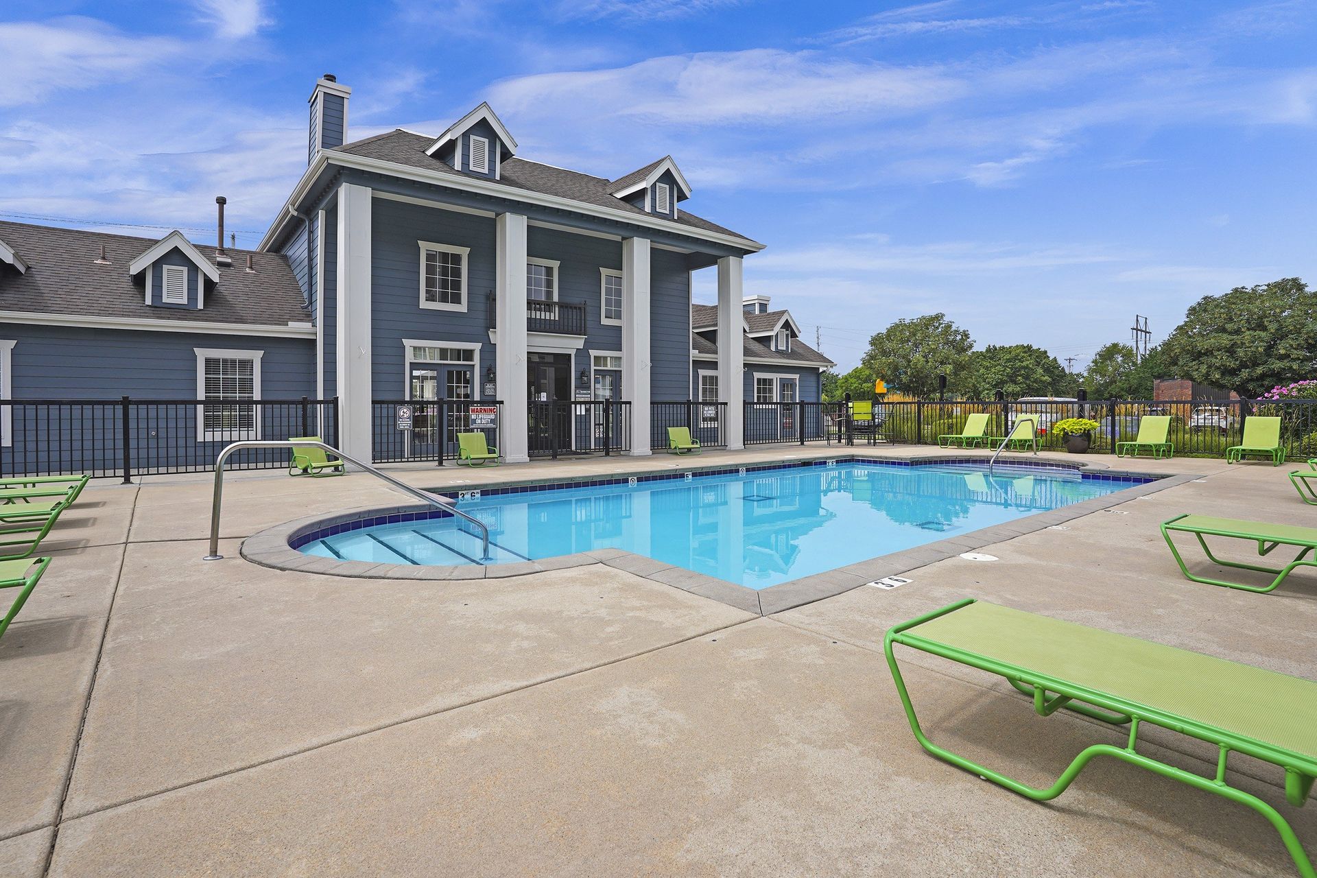 A large swimming pool is surrounded by a green bench and a grey house.