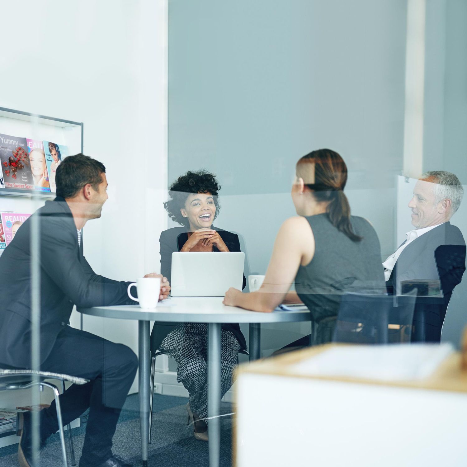 Business colleagues in a meeting at a table, smiling and collaborating inside a glass-walled office.