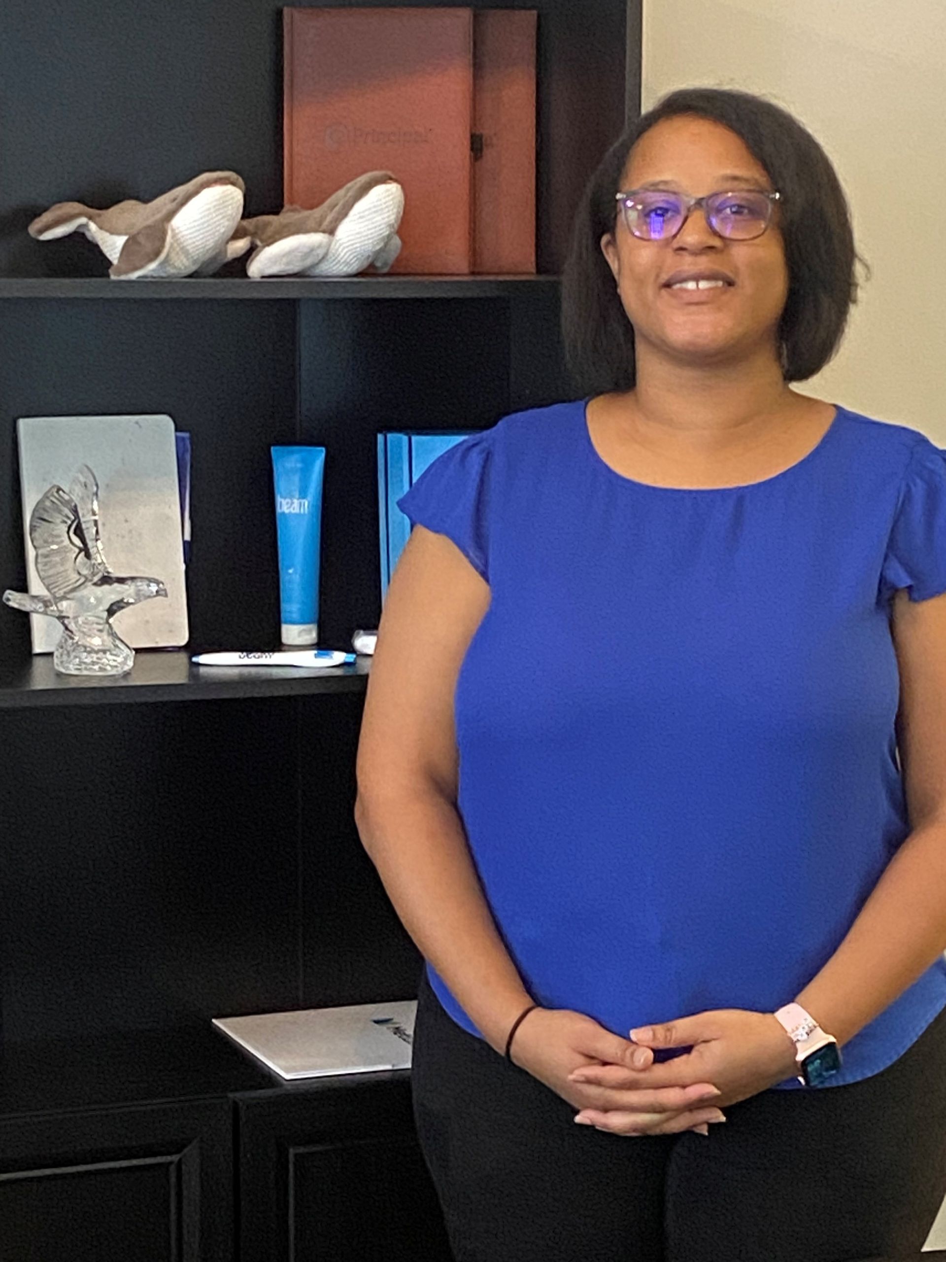 Woman with glasses in a blue top standing in front of a bookshelf.