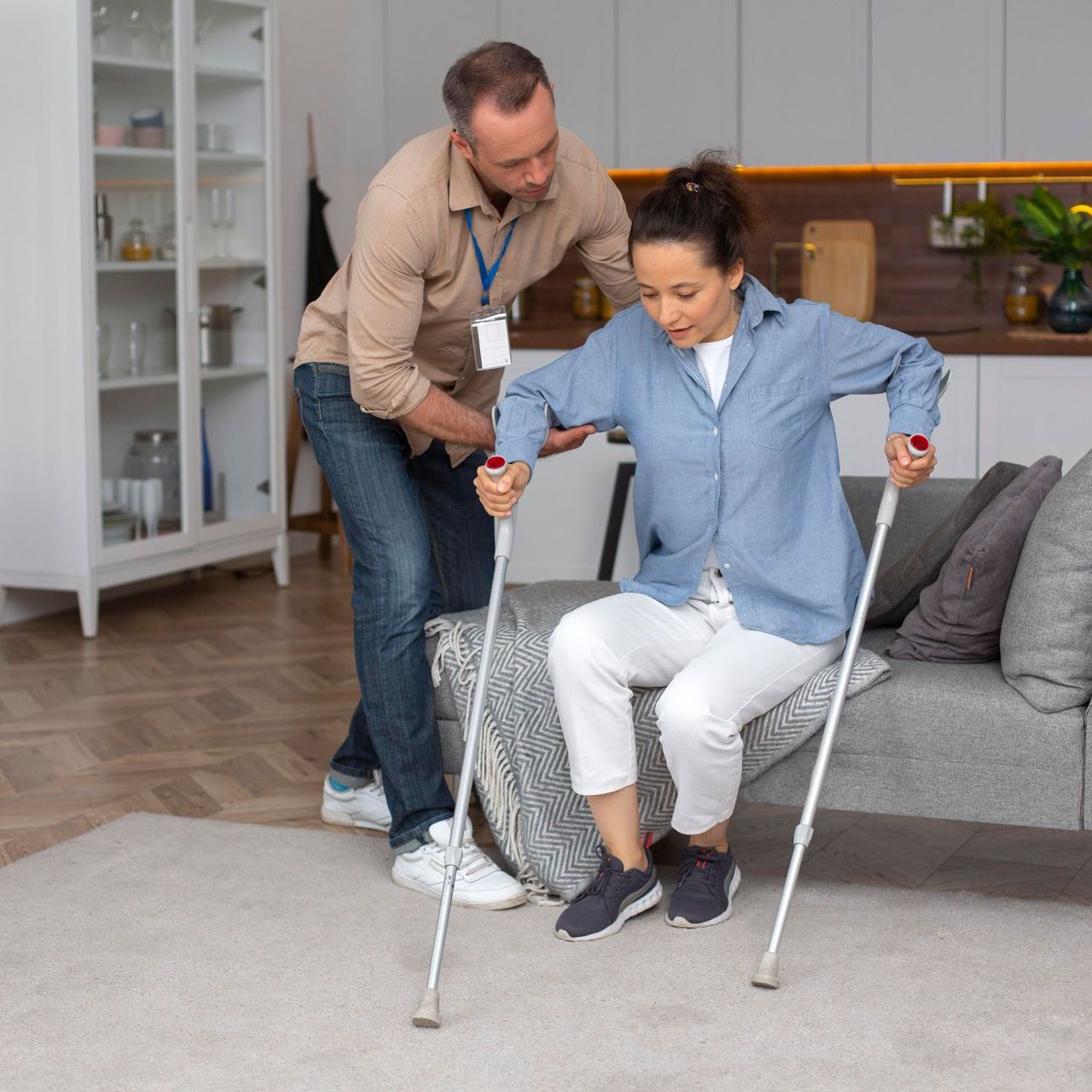 A man is helping a woman with crutches sit on a couch