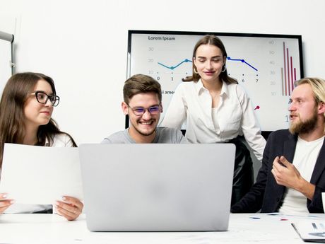 A group of people are sitting around a table looking at a laptop computer.