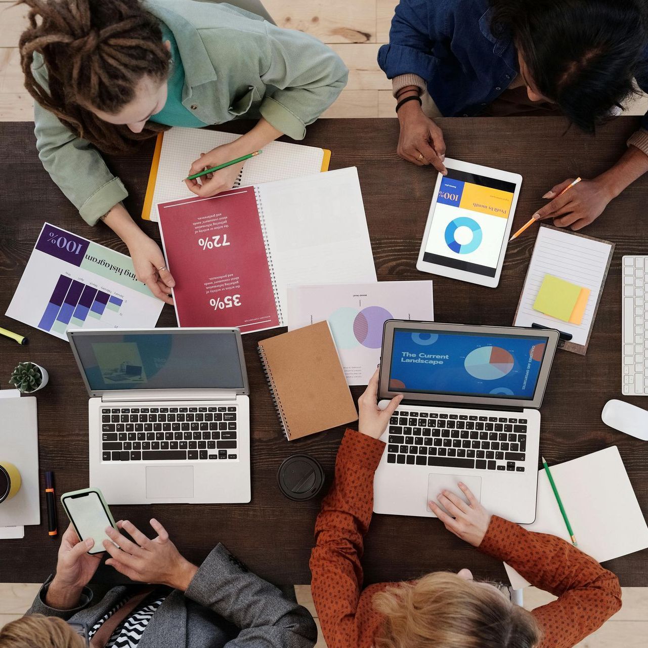 A group of people are sitting around a table with laptops and papers.