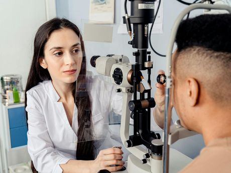 A woman is examining a man 's eye with a microscope.