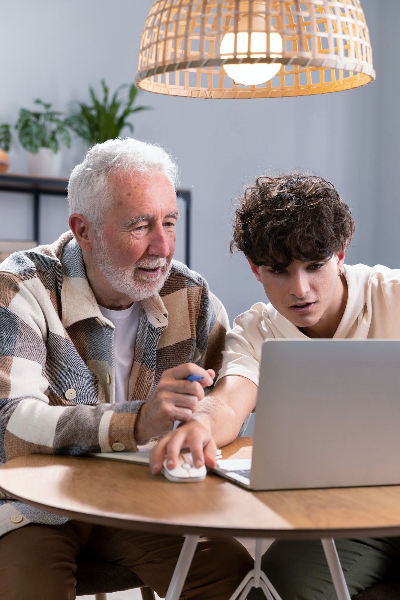 An elderly man and a young man are sitting at a table looking at a laptop computer.