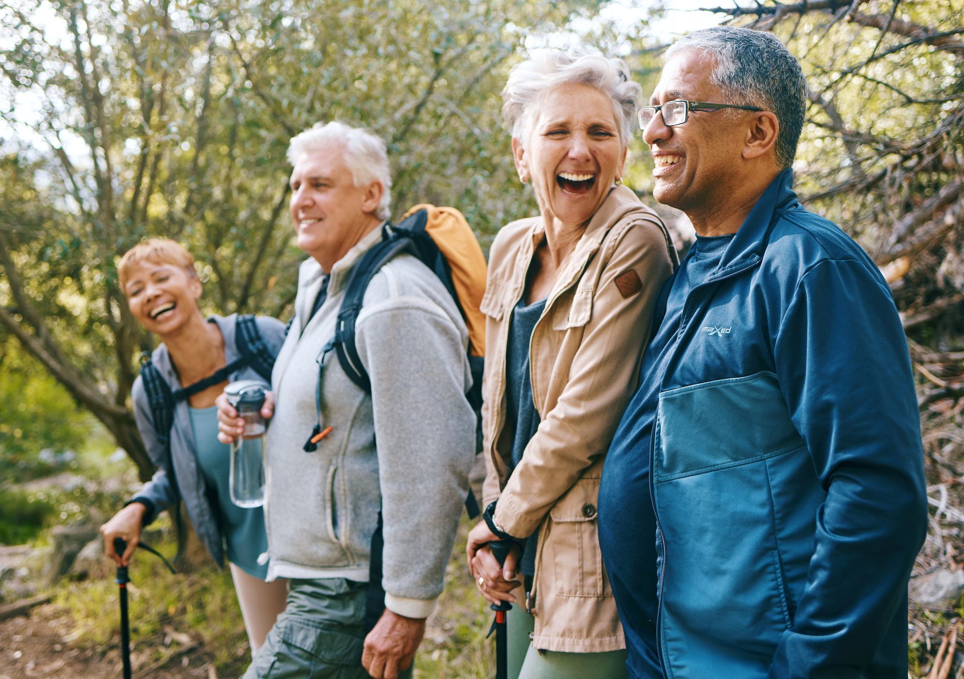A group of elderly people are hiking in the woods and laughing.