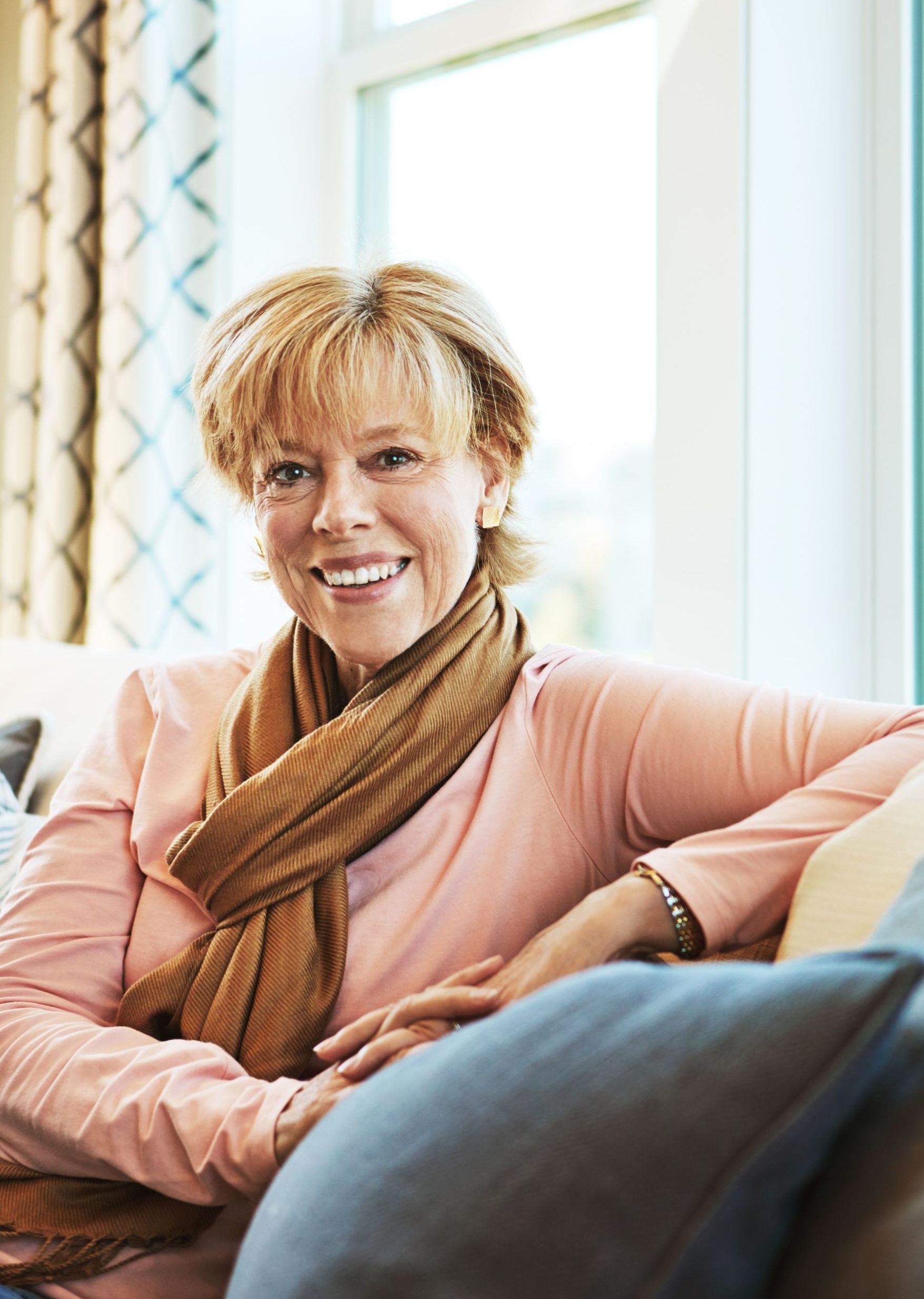 A woman is sitting on a couch wearing a scarf and smiling.