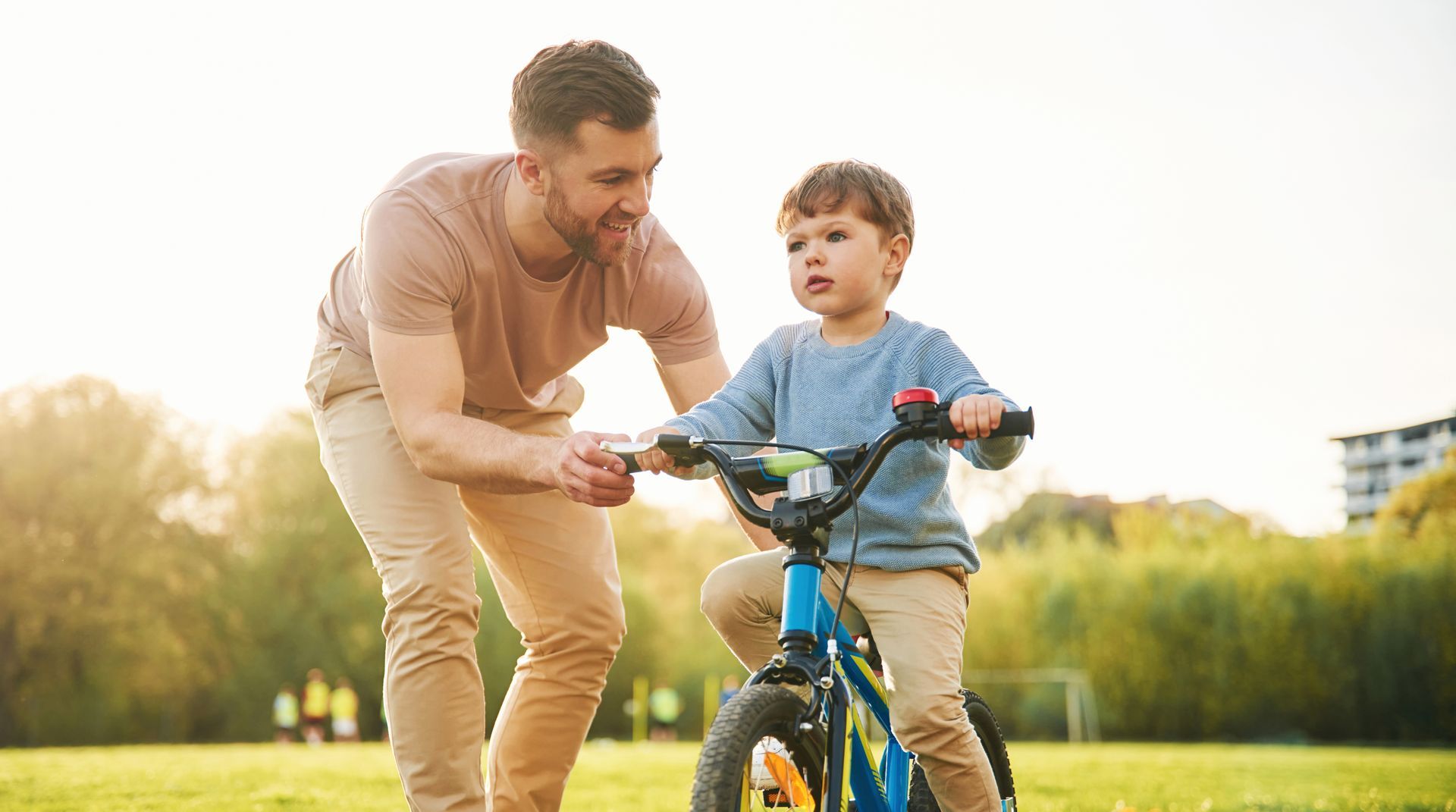 A man is teaching a young boy how to ride a bike in a park.