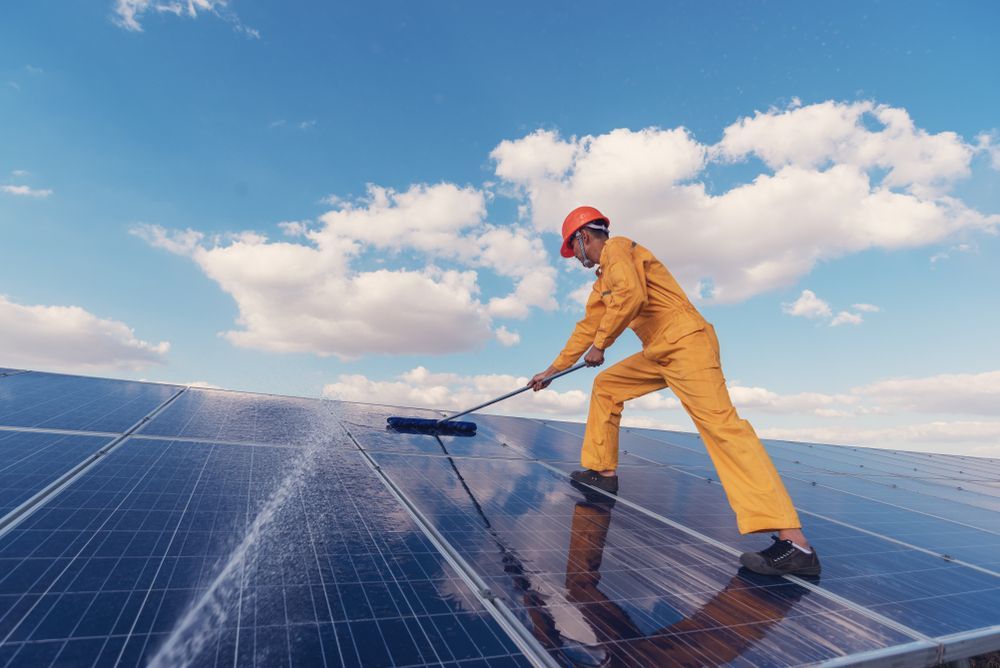 A Man Is Cleaning Solar Panels With A Broom — Hunter Smart Solar Cleaning In Maitland, NSW