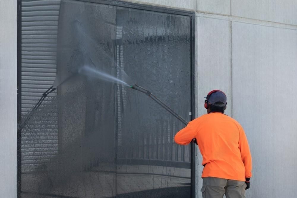 A man in an orange shirt is cleaning a door with a high pressure washer.