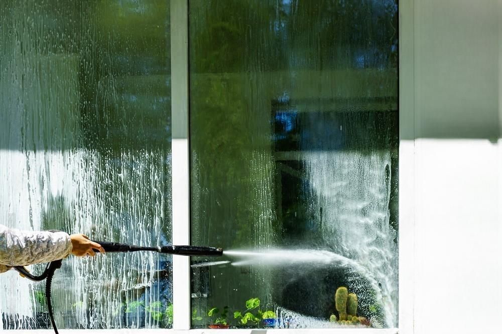 A person is cleaning a window with a high pressure washer.