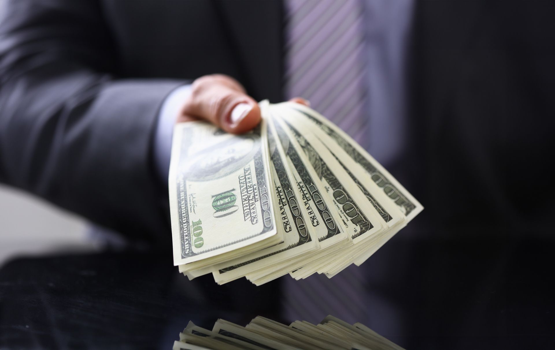 Man in suit and tie hold in arm pack of hundred dollar.