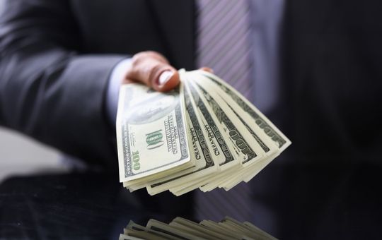 Man in suit and tie hold in arm pack of hundred dollar.