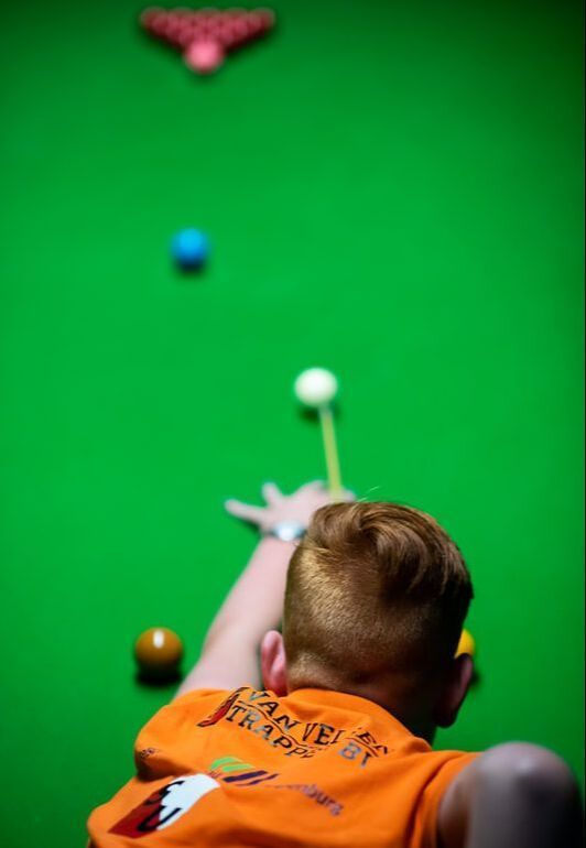 Snookerspeler in een oranje shirt bereidt zich voor op een groene tafel.