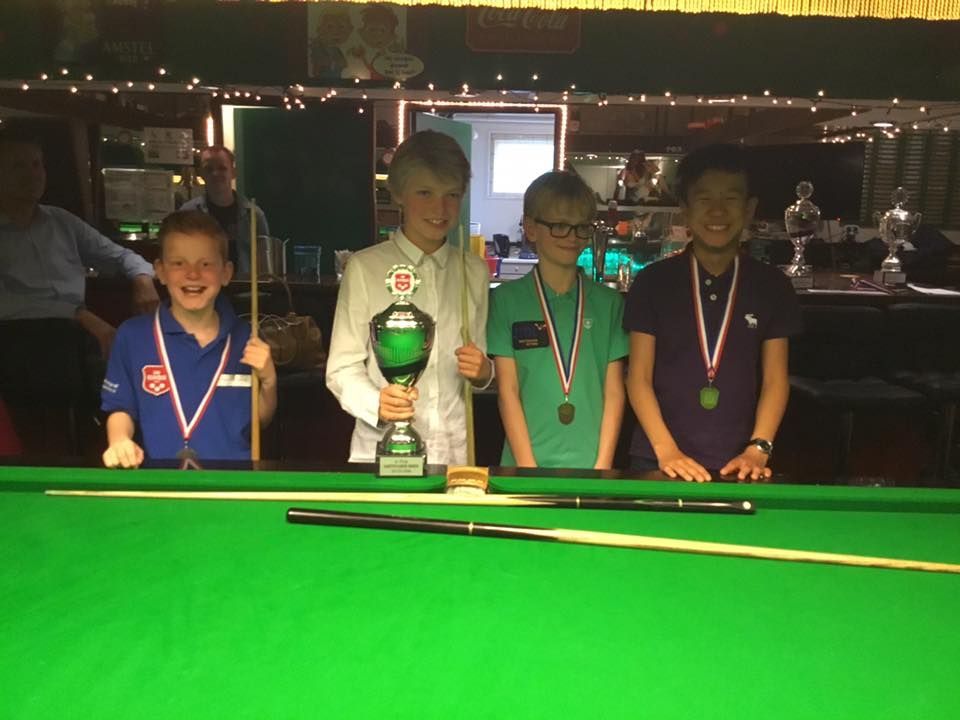 Jonge snookerspelers op een groene tafel, lachend met medailles en een trofee in een club.