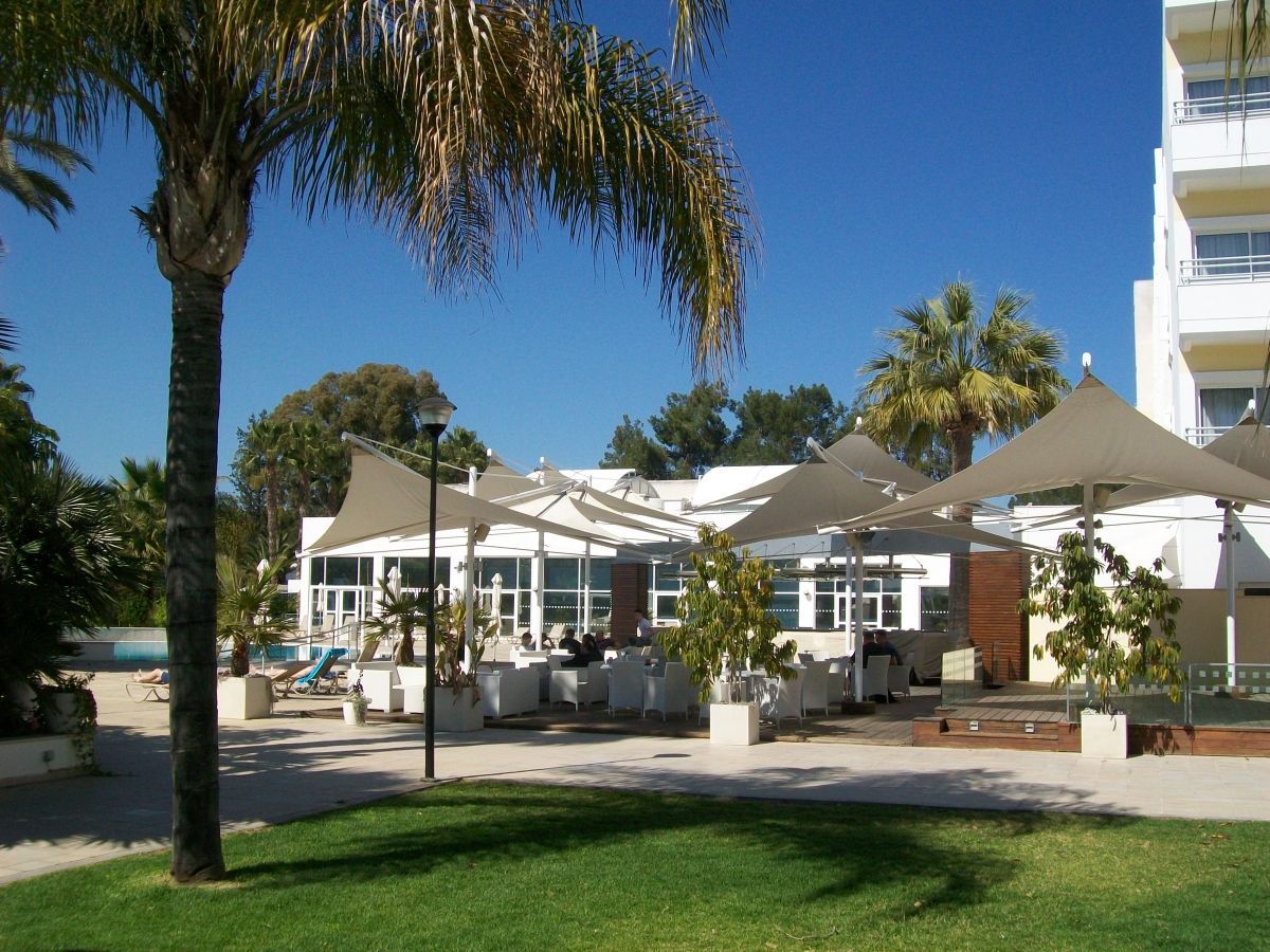 Een restaurant met terras, palmbomen en een wit gebouw onder een stralendblauwe lucht.