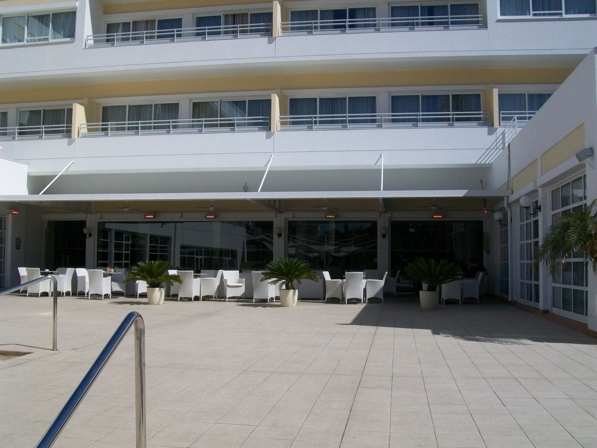 Buitenterras met witte tafels en stoelen onder een witte luifel, vlak bij een gebouw.