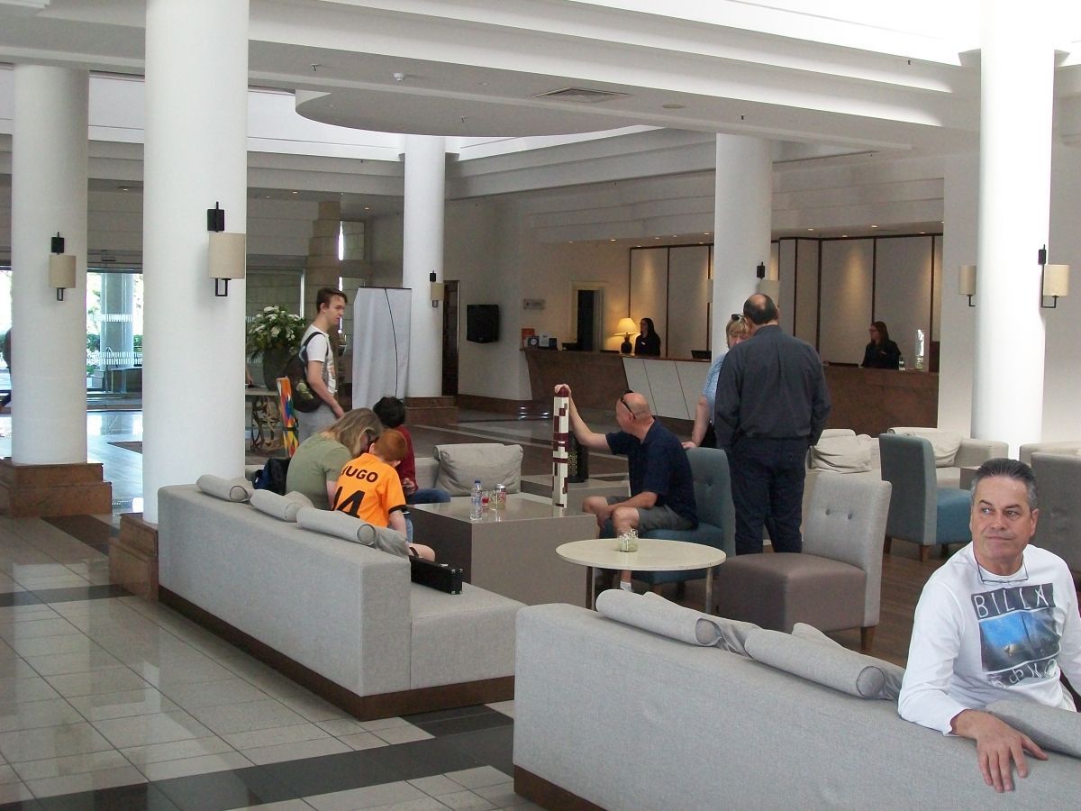 Hotellobby met mensen. Mannen en kinderen ontspannen op banken, bij de receptie en de zuilen.