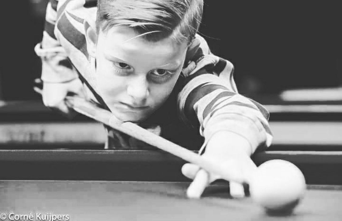 Boy concentrates as he takes a billiards shot, aiming cue at white ball. Black and white photo.
