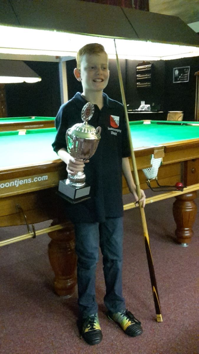 Lachende jongen met trofee en snookerkeu in zijn hand bij een snookertafel.