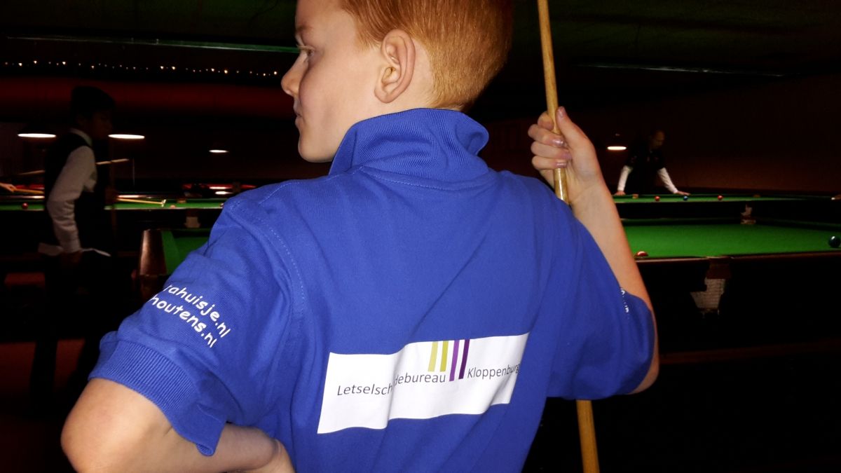 Jongen in een blauw shirt met een biljartkeu in een snookerhal.