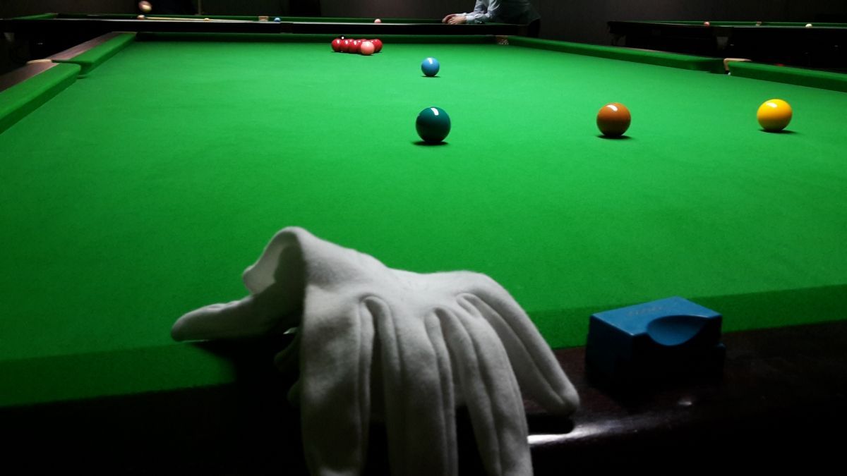Een snookertafel met gekleurde ballen, een keu en een speler, met een witte handdoek en blauw keu-krijt aan de zijkant.