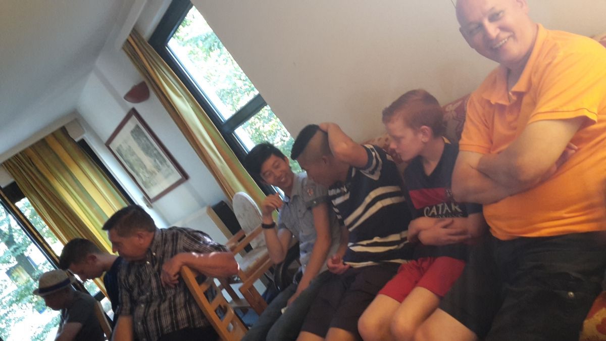 Een groep mensen binnen, sommigen zittend. Eén man zingt in een microfoon. Anderen lijken te luisteren.