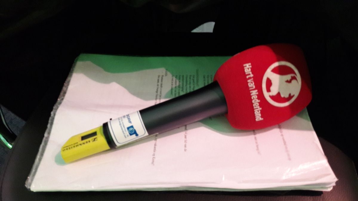 Rode microfoon met logo op een stapel witte papieren, in een voertuig.