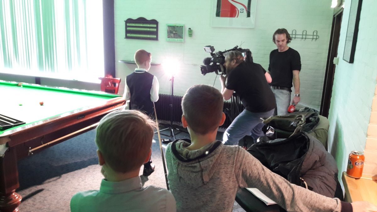 Kinderen filmen een scène met een videocamera in een kamer met een pooltafel. Een crewlid bedient de camera.