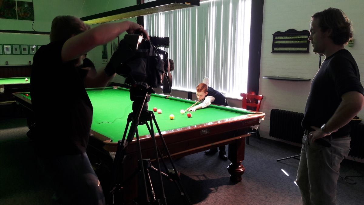 Een videoploeg filmt iemand die snooker speelt op een groene tafel in een snookerhal.