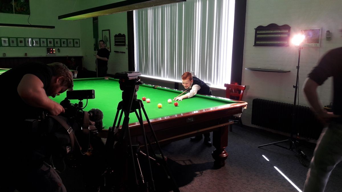 Man in pak speelt pool, gefilmd door een crew in een goed verlichte kamer.