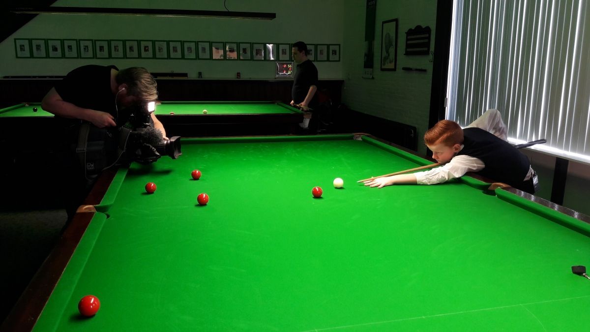 Een persoon richt een speelbal op een groene snookertafel, terwijl anderen toekijken.
