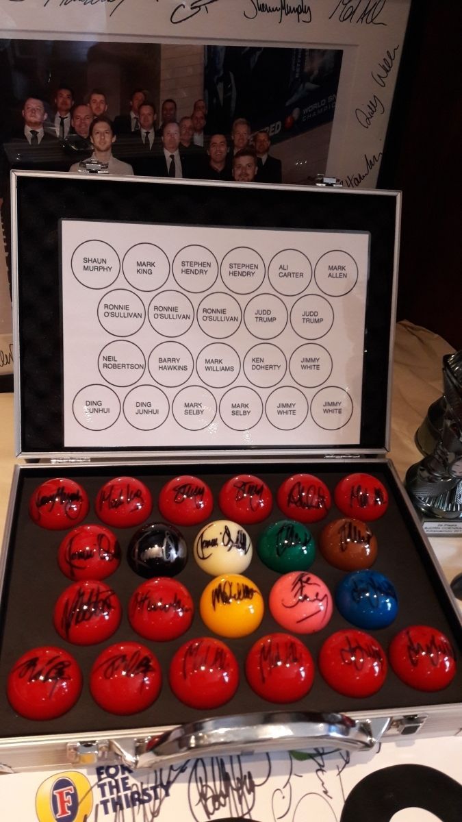 Een doos met poolballen en een papiertje met cirkels. De ballen zijn rood, wit en andere kleuren. Een gesigneerde foto op de achtergrond.