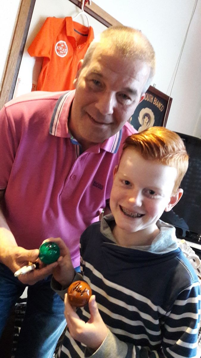 Man en jongen houden beschilderde eieren vast, lachend. Oranje shirt op de achtergrond.