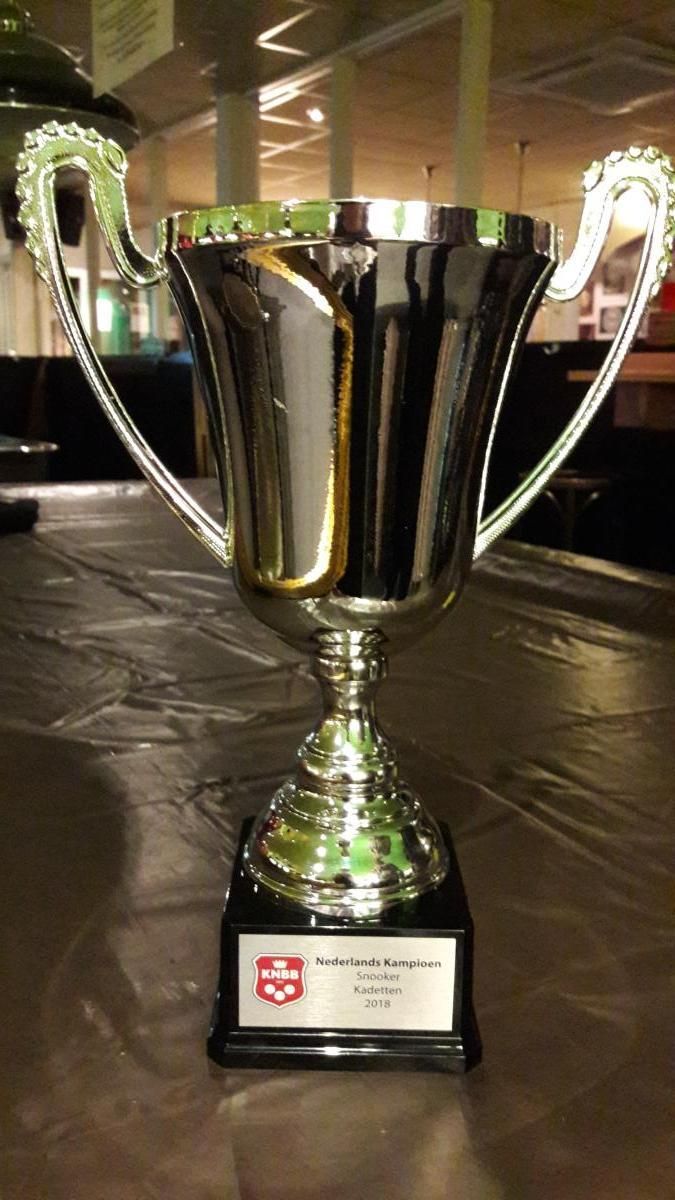 Zilveren trofeebeker met zwarte voet op tafel.