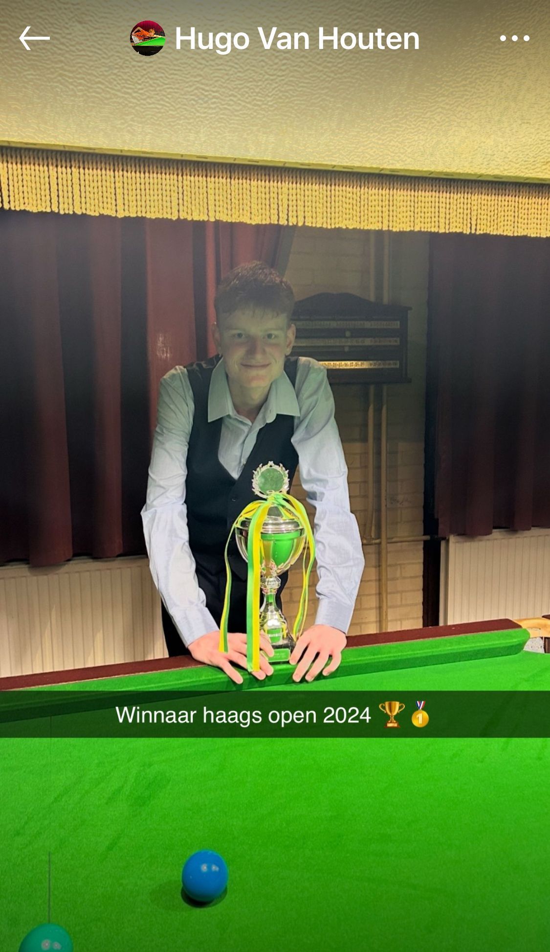 Een jongeman met een trofee op een groene pooltafel. Tekst: 