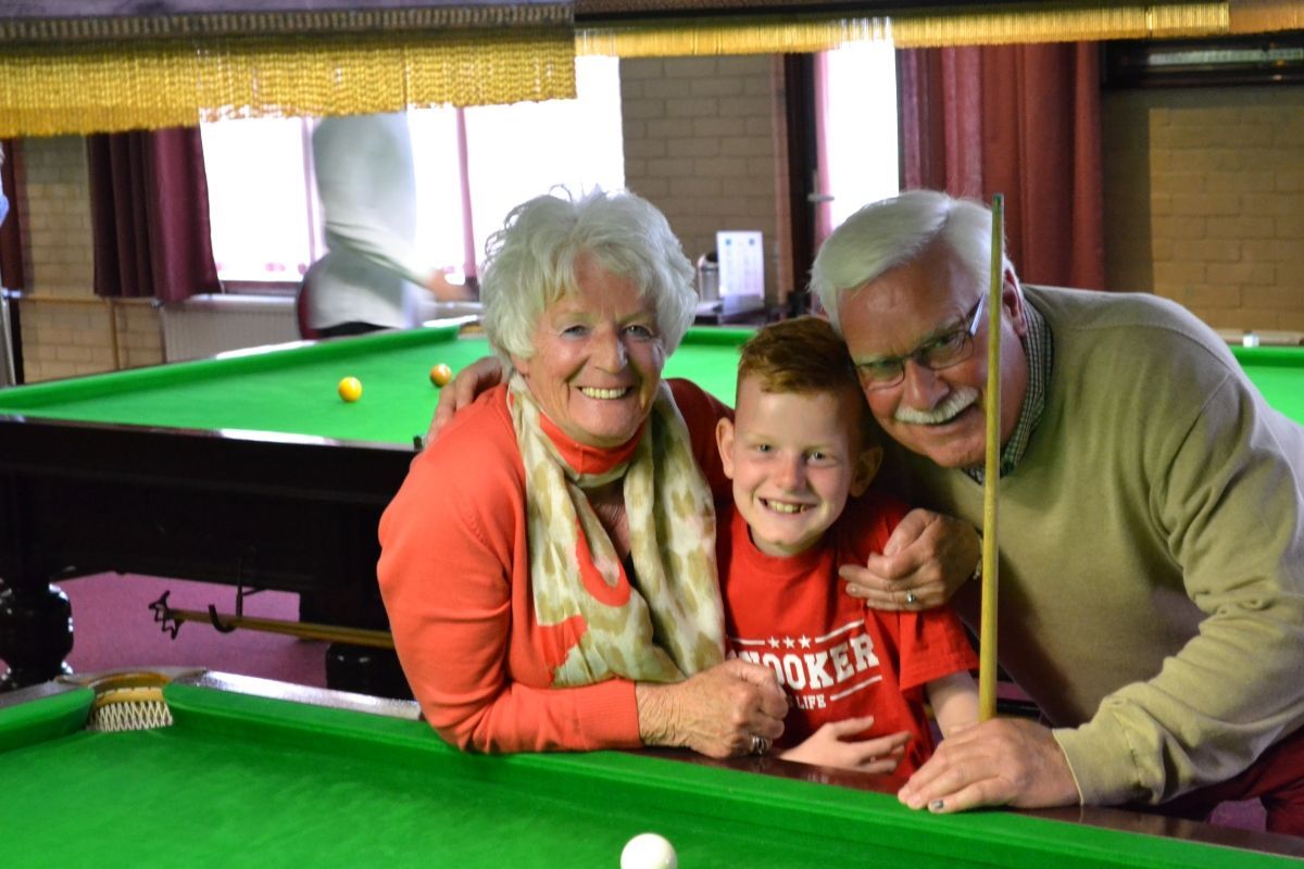 Grootouders poseren met een kind bij een snookertafel en lachen.