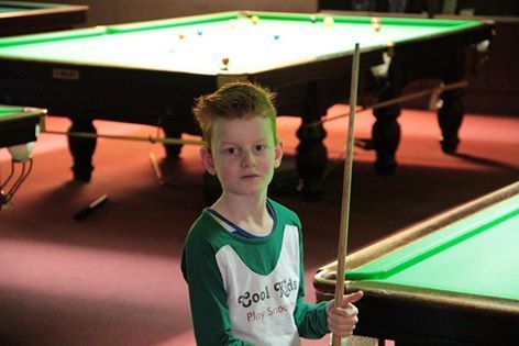 Jongen met rood haar en een keu in een snookerhal.