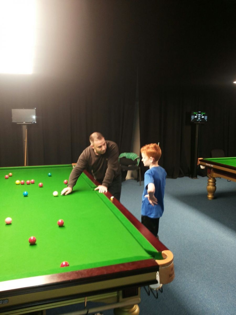 Man leert een jonge jongen snookeren op een groene tafel van vilt. Binnen, met weinig licht.