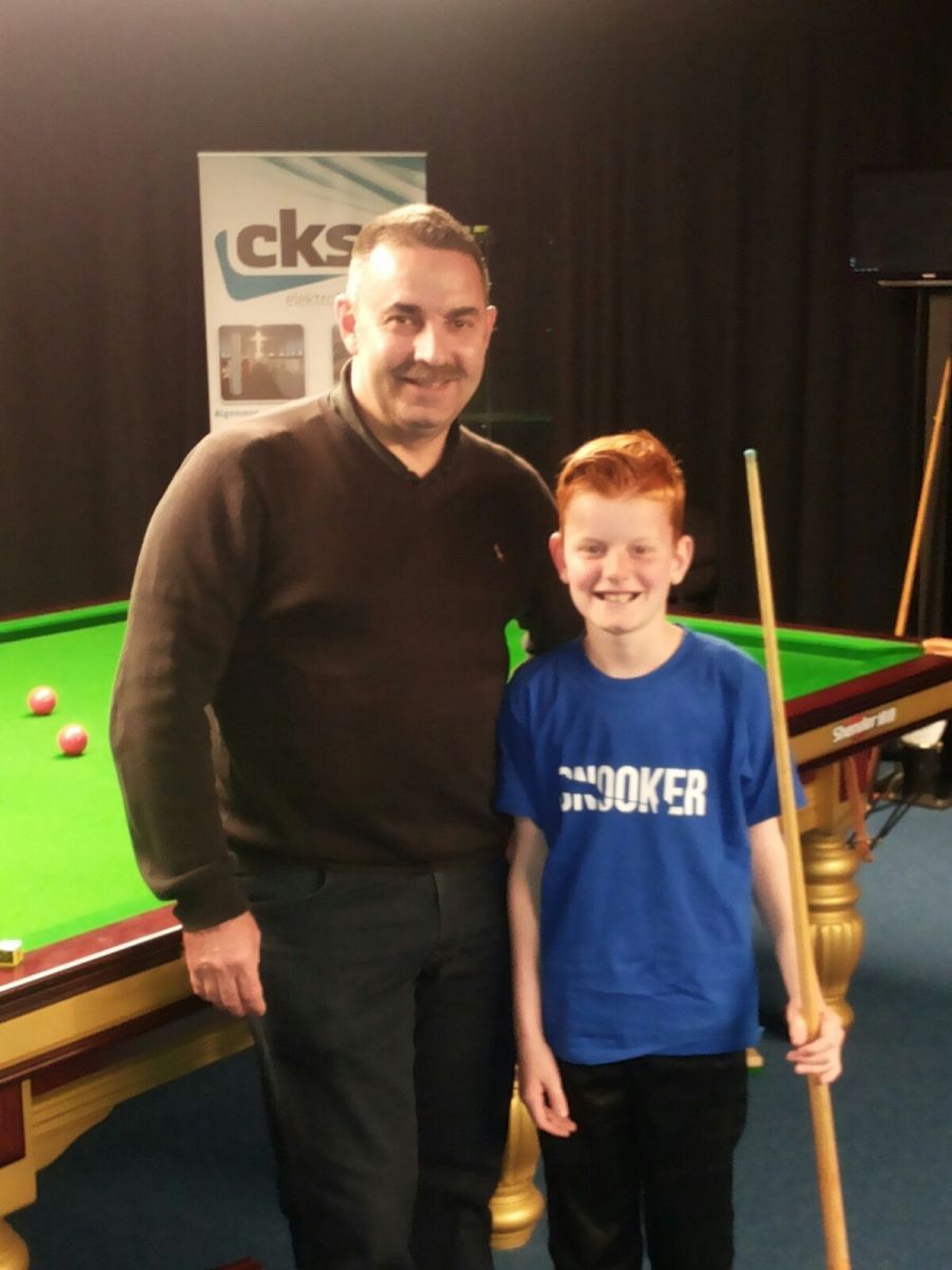 Man en jongen in een snookerkamer; de jongen houdt een keu vast. Beiden lachen bij een pooltafel.